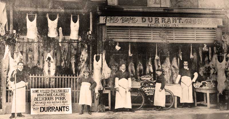 Butcher's shop in London in 1910, showing pork and beef hanging in the shop window and open to the street. Standing outside are the butcher, his assistants and a very young delivery boy with his bike.
