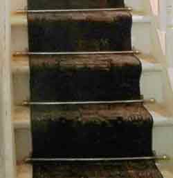 Stair carpet,1940s England: long narrow length held down at the edges of each stair with decorative rods and showing the wood of the staircase at each side