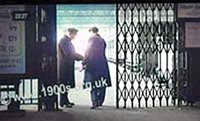 1940s train ticket inspector checking a passenger's train tickets as he enters a platform at a large city rail terminus