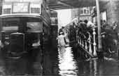 Flooding c1920: passengers getting on a bus via a plank