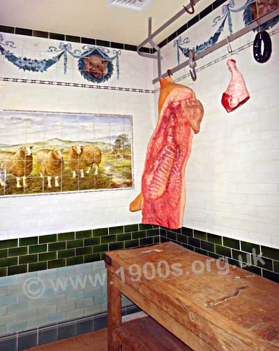 Inside a butcher's shop in the early 1900s, showing the sides of meat hangin up, the wooden chopping board and the tiled walls