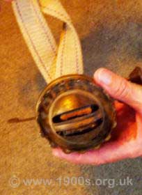 Looking down on part of an old dismantled oil lamp with two wicks, showing the support that held the wicks such that short lengths were kept above the surface of the paraffin oil.