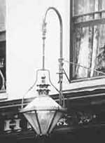 A typical privately-owned gas lamp suspended outside, over a shop window and contributing
to the illumination of the streets in the early 1900s.