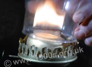 Glass chimney of an oil lamp being put over the lighted wick